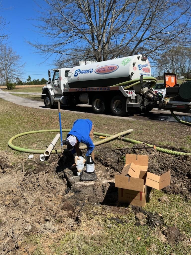 Man working on septic system. A truck with a tank is parked nearby on a sunny day.