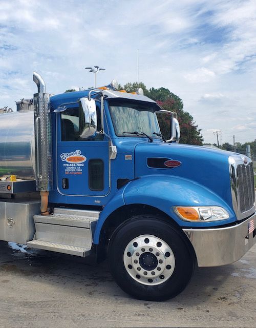Blue tanker truck parked with a shiny chrome exhaust pipe and a light blue sky.