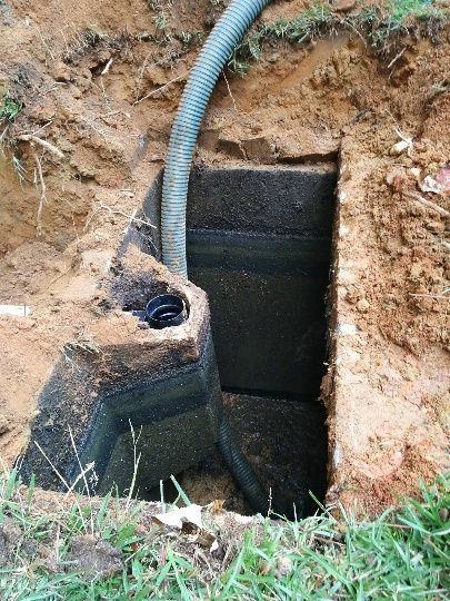 Open utility pit in dirt with a gray corrugated hose and black lining beside grass Open utility pit in dirt with a gray corrugated hose and black lining beside grass