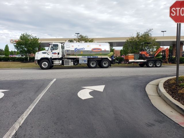 White tanker truck and trailer with equipment, parked at a stop sign.