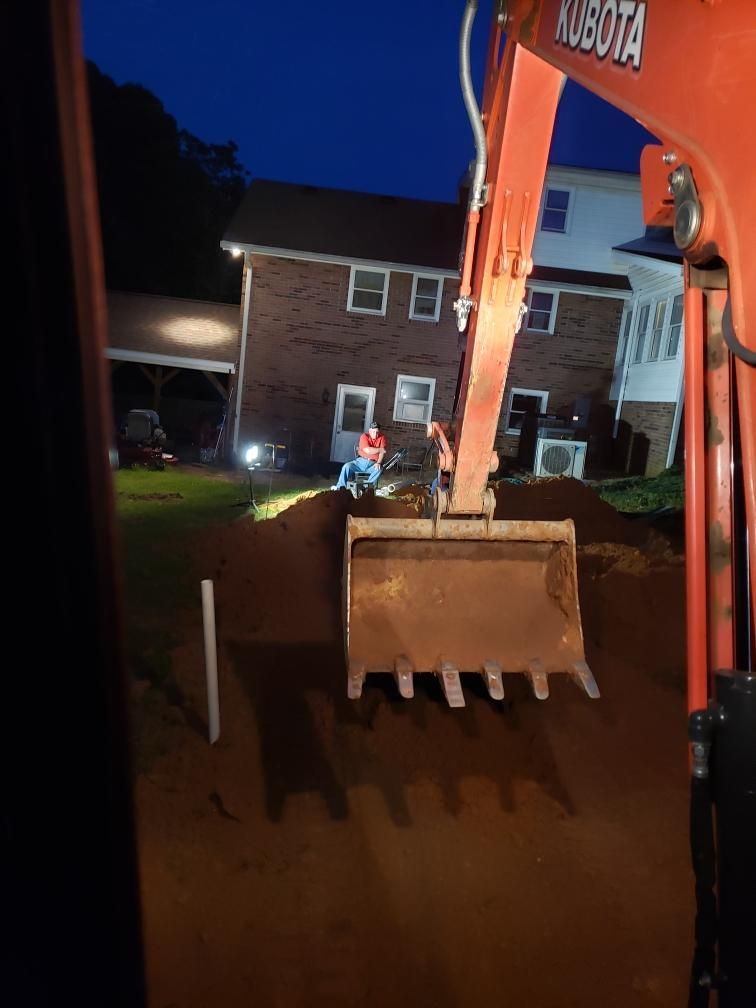 An excavator bucket in front of a house at dusk. A person works in the distance.