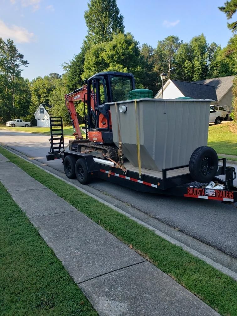 Orange excavator on a trailer with a large gray tank, parked on a residential street.