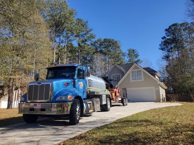 Blue tanker truck parked on a driveway in front of a house, sunny day.