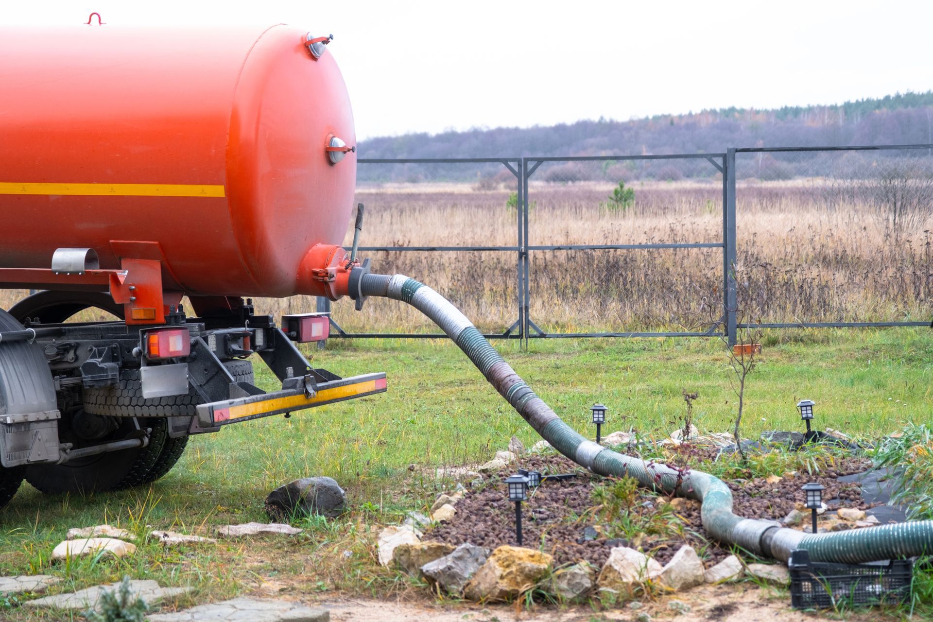Orange septic tank truck with hose discharging waste onto a lawn.