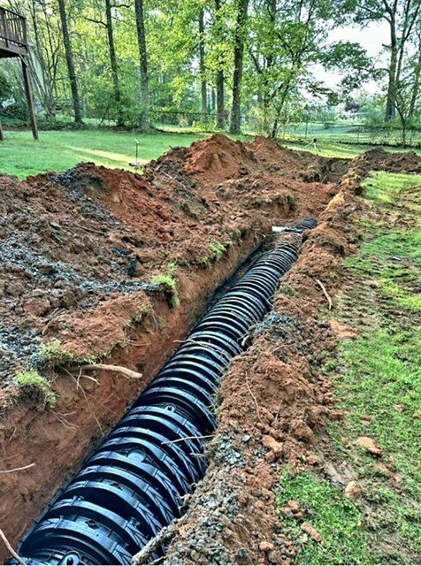 Black corrugated pipe in a trench; construction site in a grassy area with trees in background.
