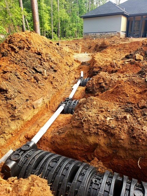 Trenches with buried septic system components and white PVC piping, outdoors.