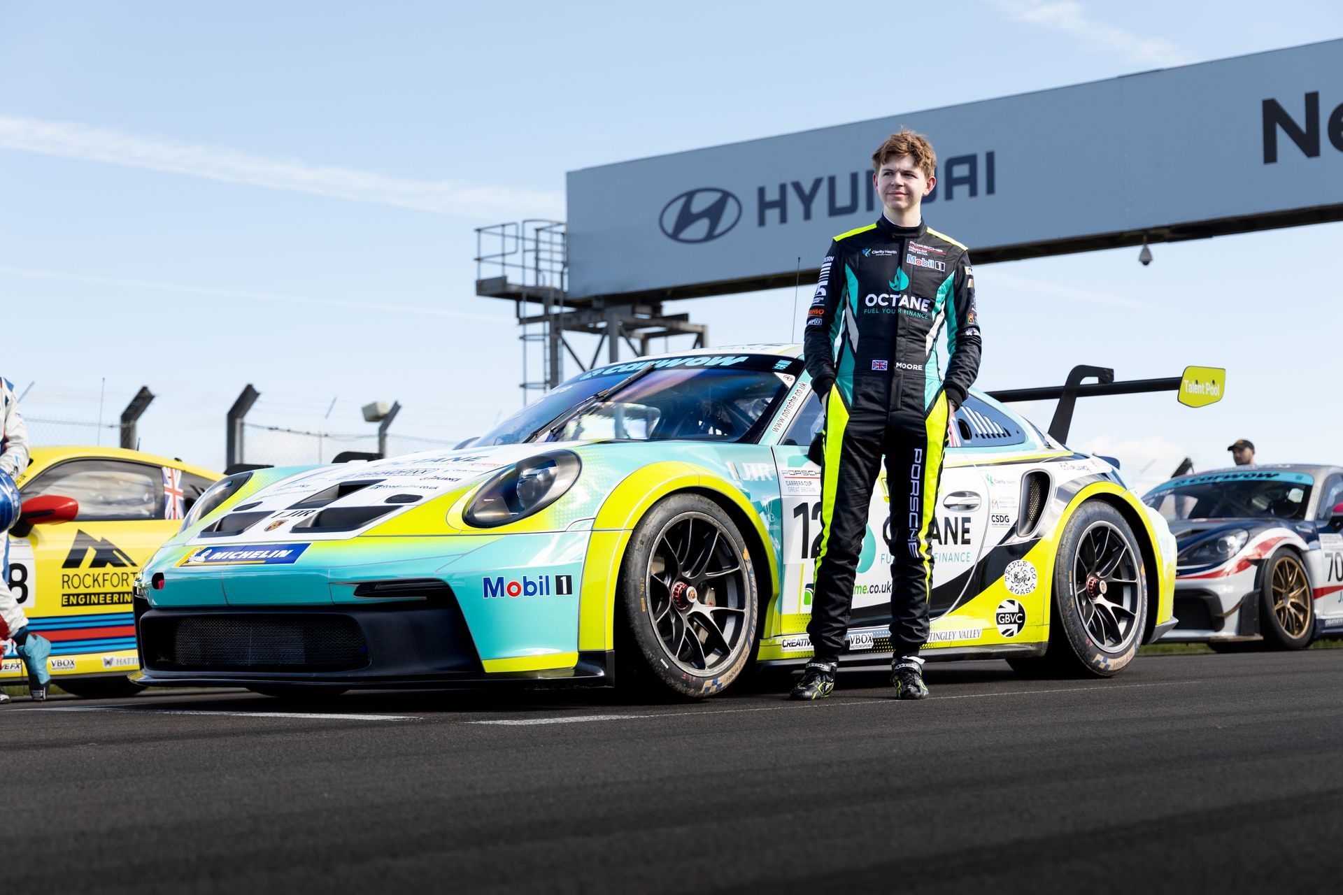 Jonny Moore Motorsport porsche carrera cup race car in pits with Jonny stood next to it 