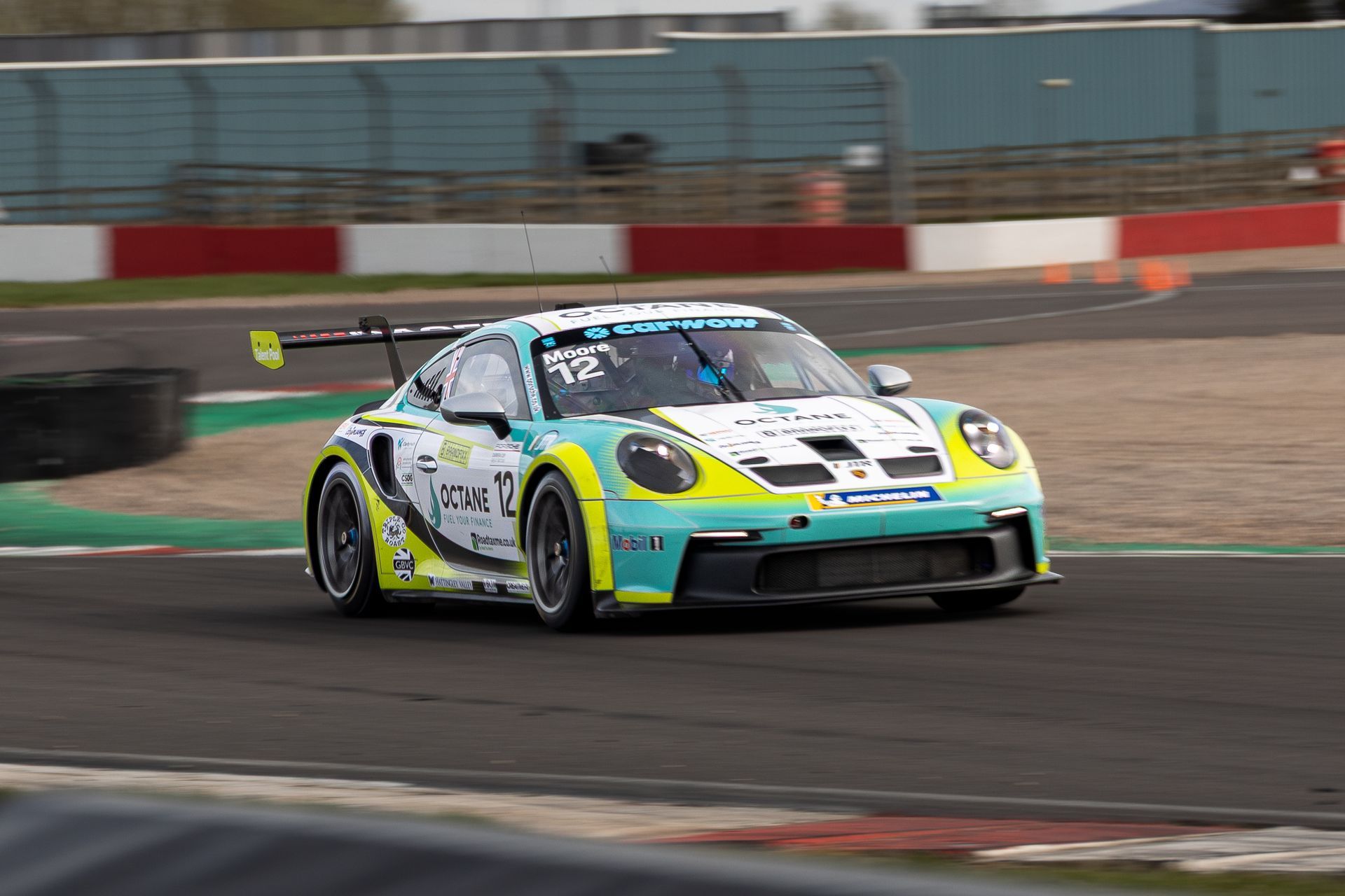 Colorful race car speeding around a track corner with red-and-white barriers in the background