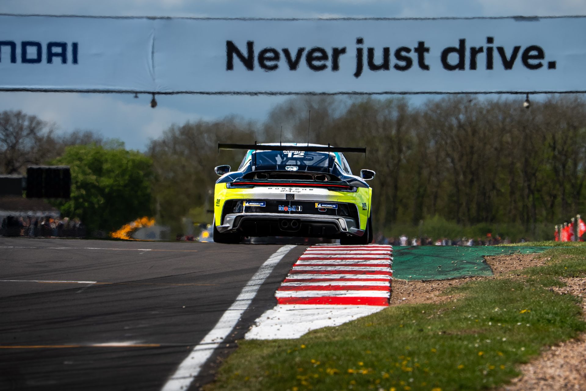 Race car airborne on a track curb under a “Never just drive” banner