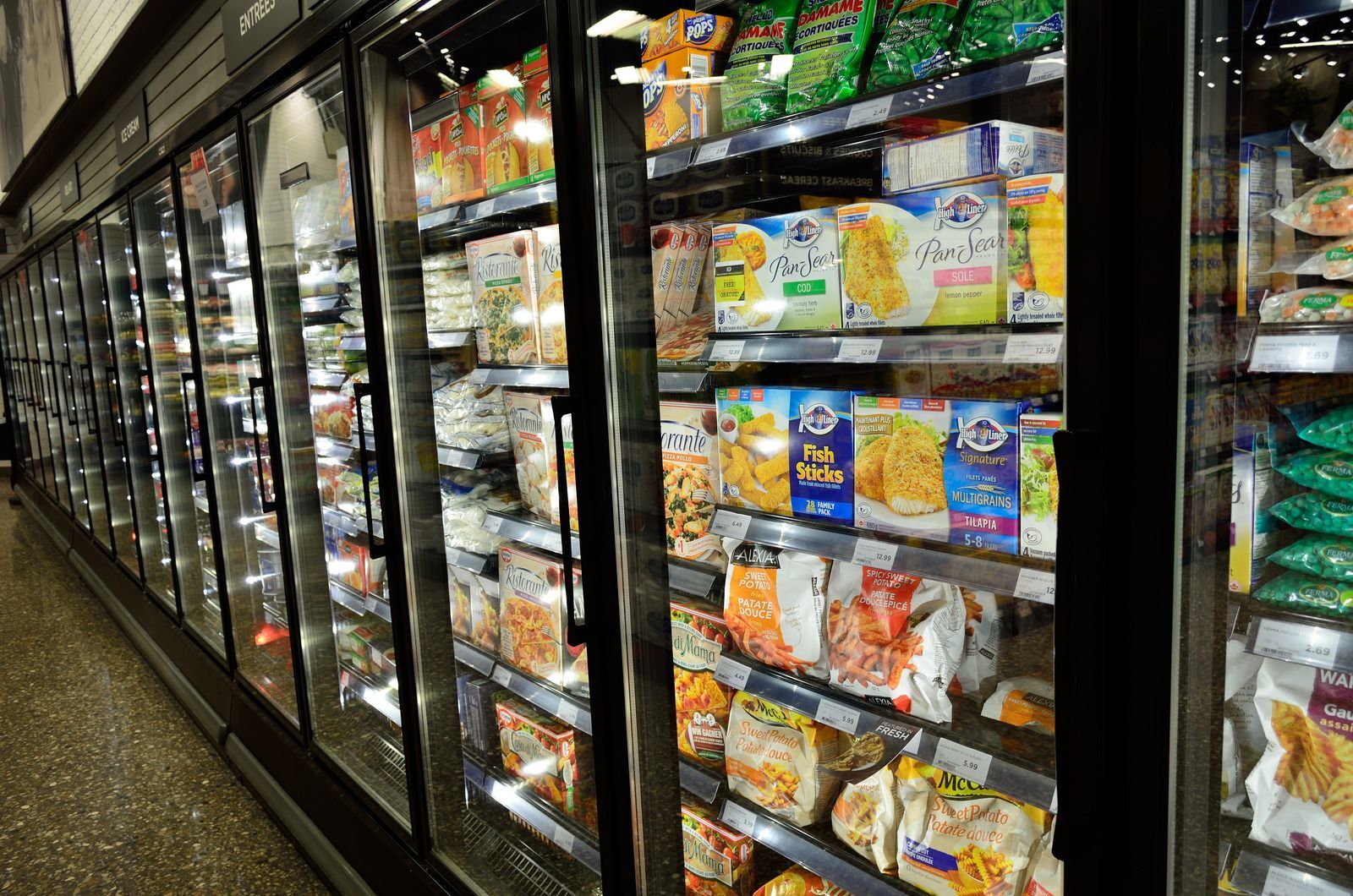 Freezer aisle in a grocery store, stocked with frozen food packages. Reflective glass doors, overhead lighting.