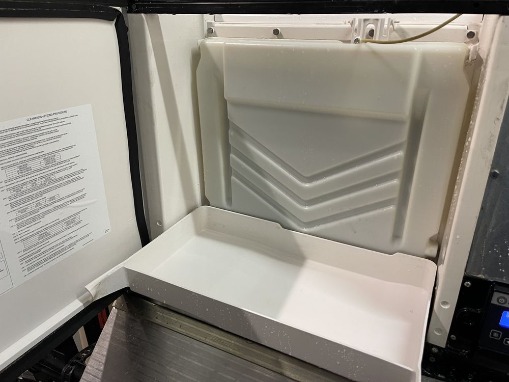 Open white tray inside a white appliance, possibly a refrigerator or ice maker.