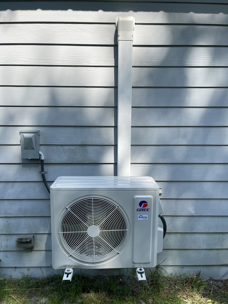 A white air conditioner unit mounted on a gray wall with white vent cover.