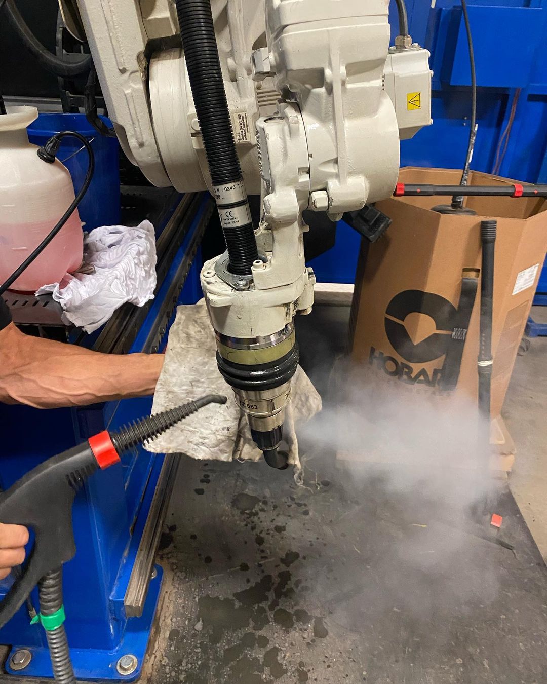 Un bras robotisé est nettoyé à la vapeur. Une personne tient la buse de vapeur. De la fumée s'échappe.
