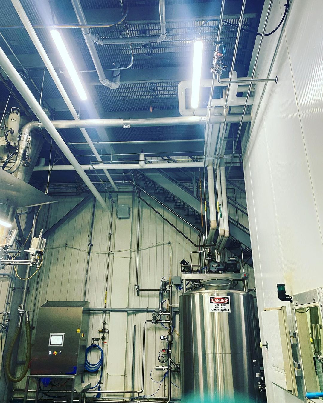 Intérieur de style industriel avec cuves, tuyauteries et panneau de commande en acier inoxydable.