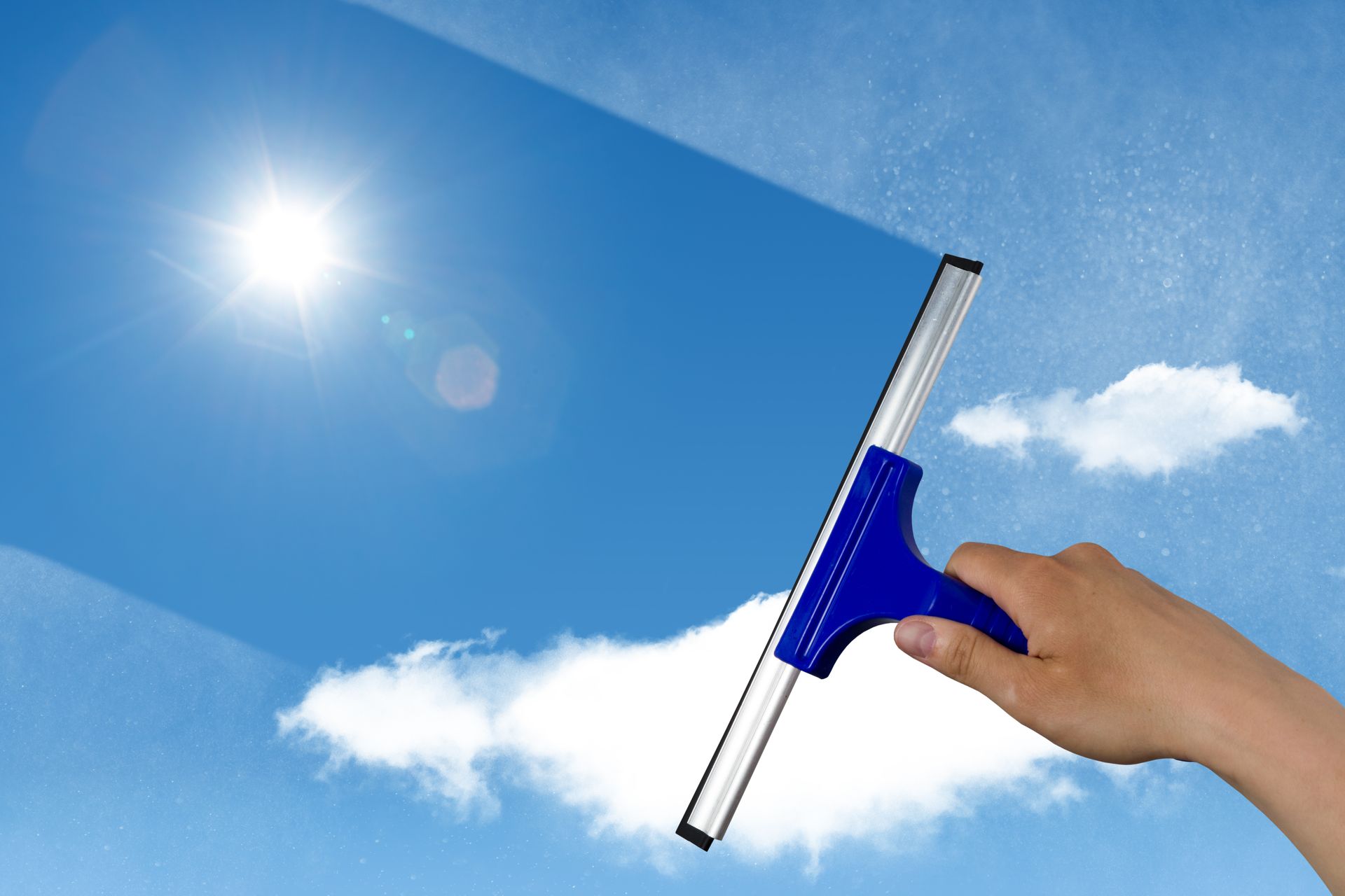 Main utilisant une raclette pour nettoyer le ciel, journée ensoleillée avec ciel bleu et nuages ​​blancs.
