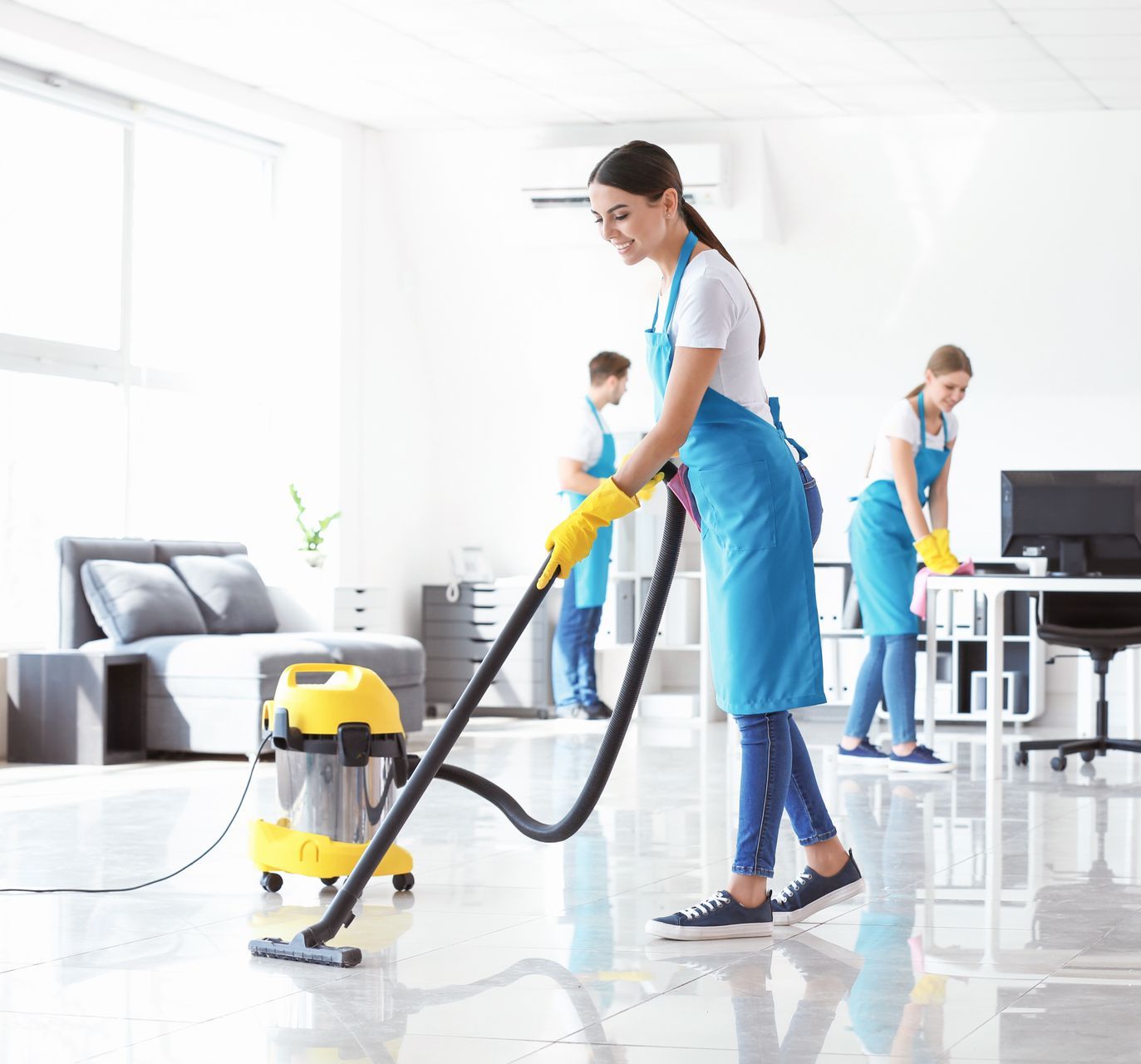 Une femme passe l'aspirateur dans un bureau, avec deux autres agents d'entretien en arrière-plan.