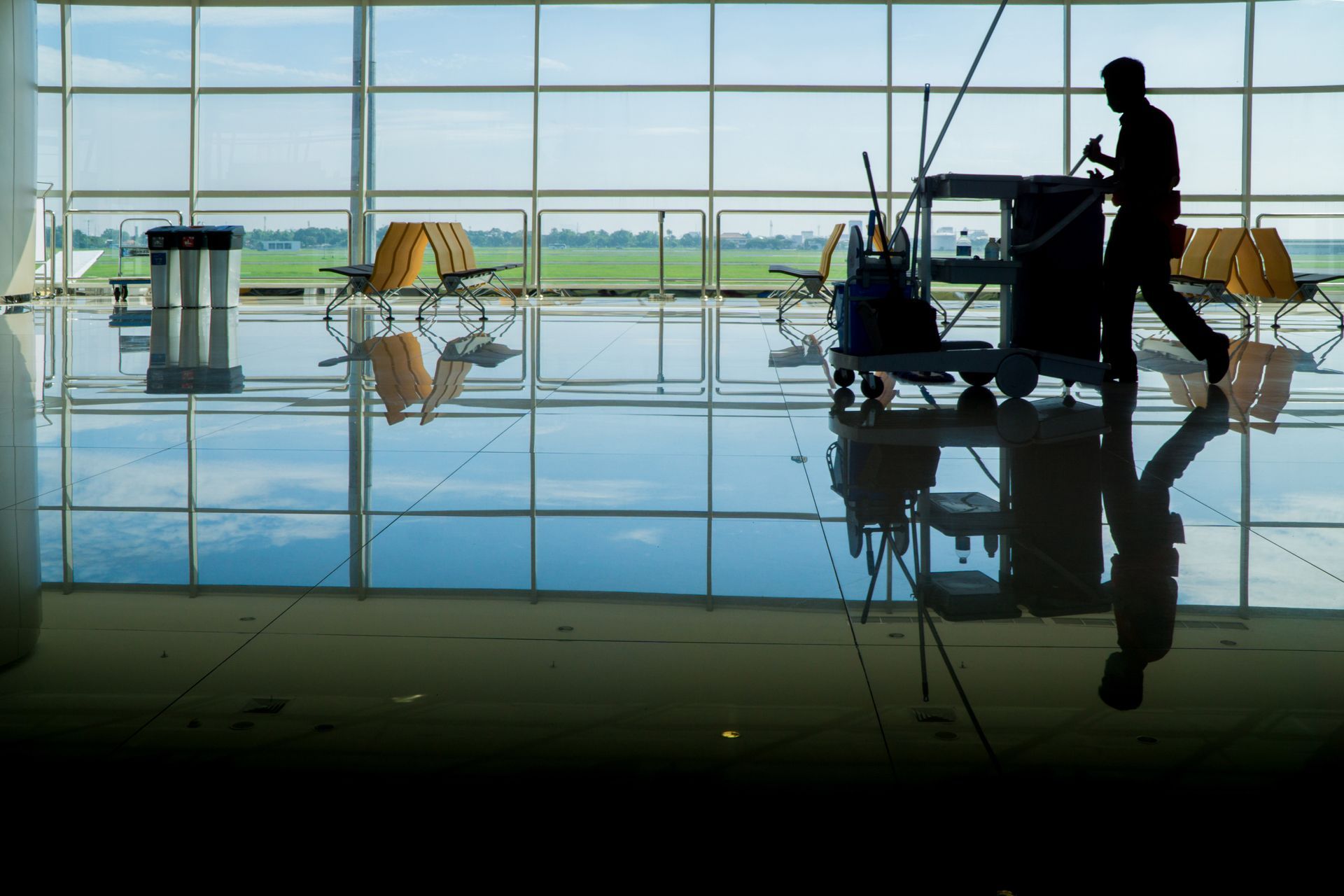 Silhouette d'une personne nettoyant un aéroport, reflétée sur le sol brillant. Chariot de nettoyage