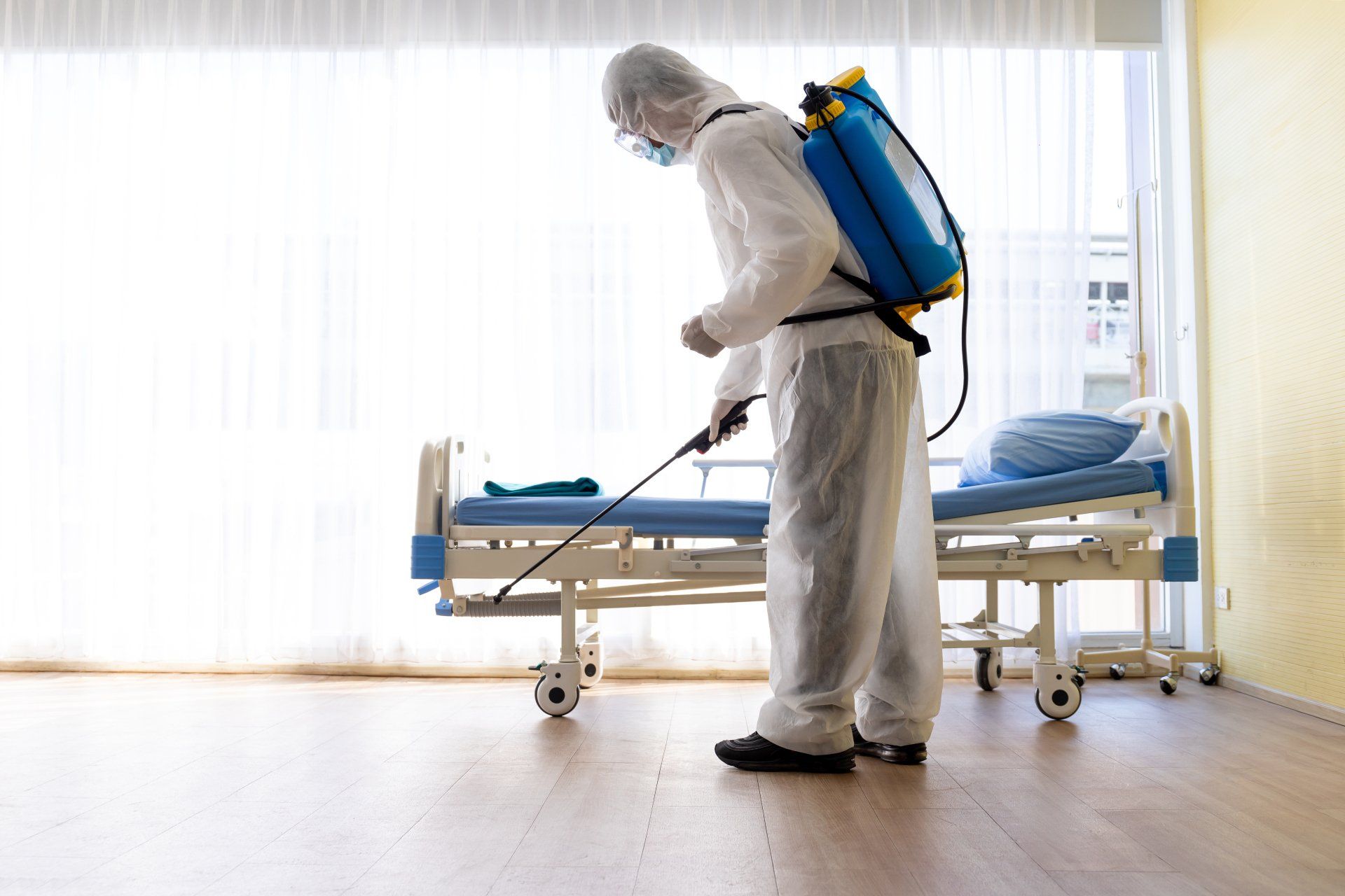 Une personne en combinaison de protection désinfecte une chambre d'hôpital avec un pulvérisateur.