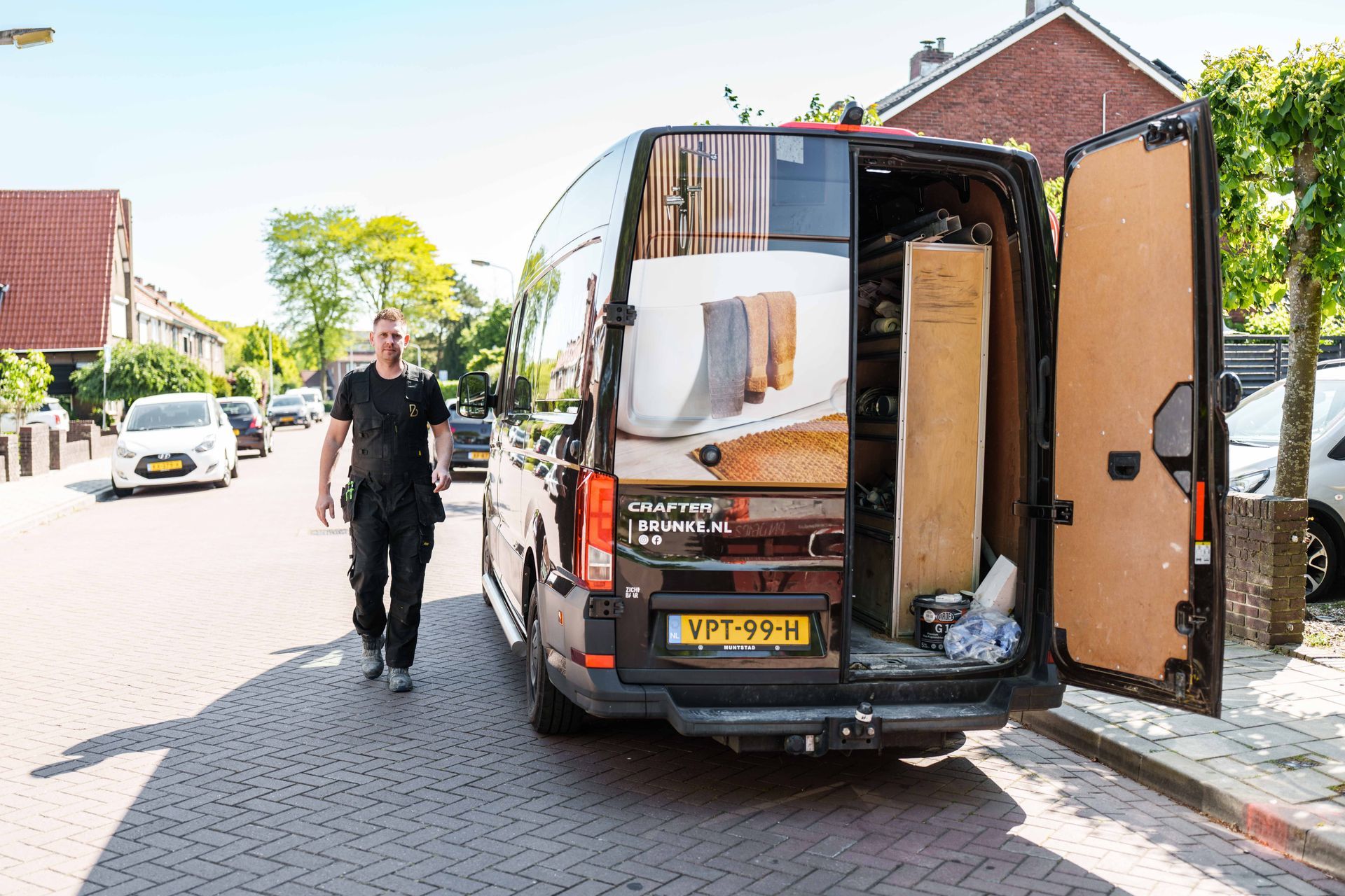 Een man laadt meubels uit een bestelbus die geparkeerd staat in een woonwijk.