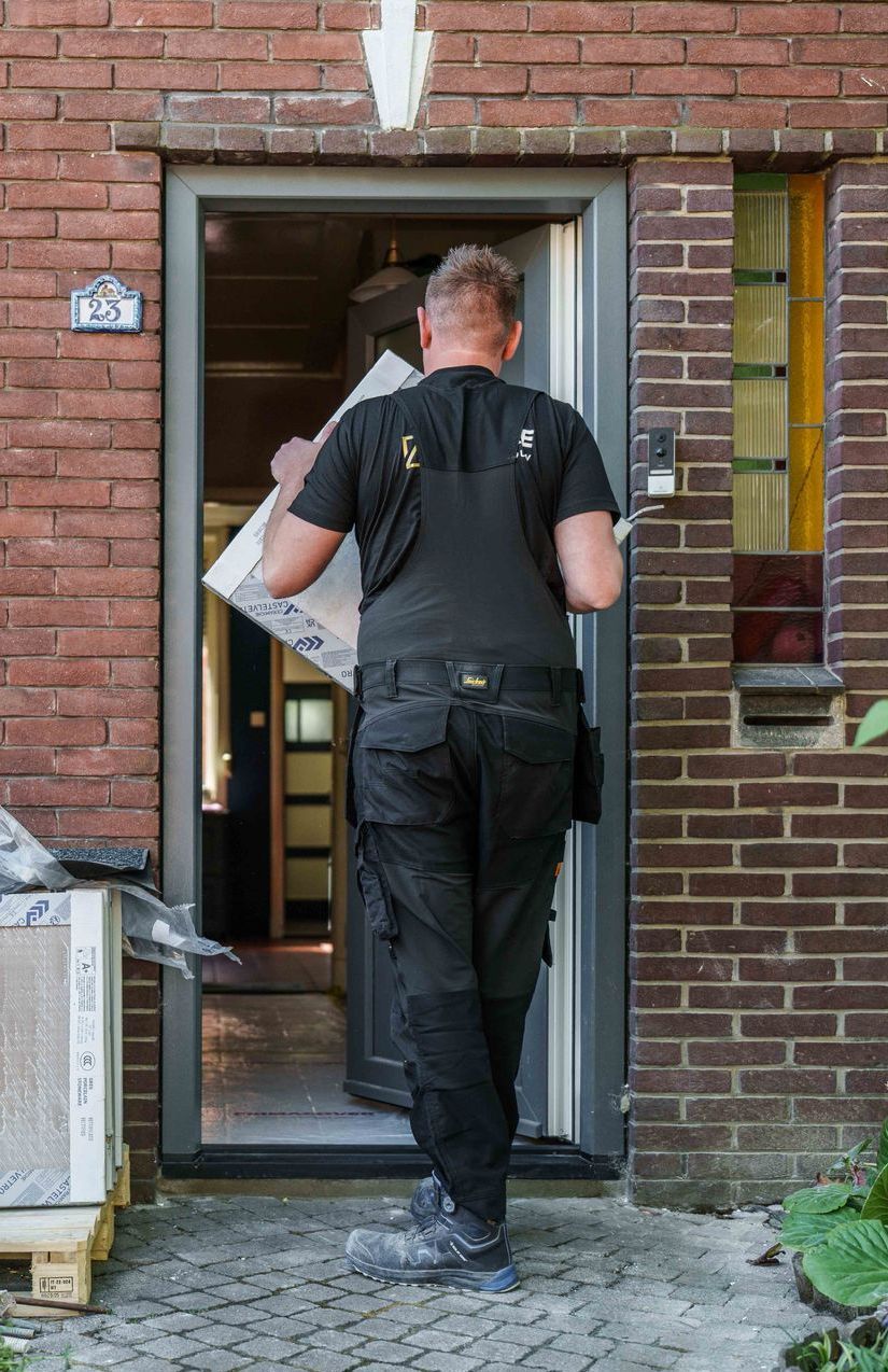 Een bezorger draagt ​​een pakket naar binnen in een bakstenen gebouw.