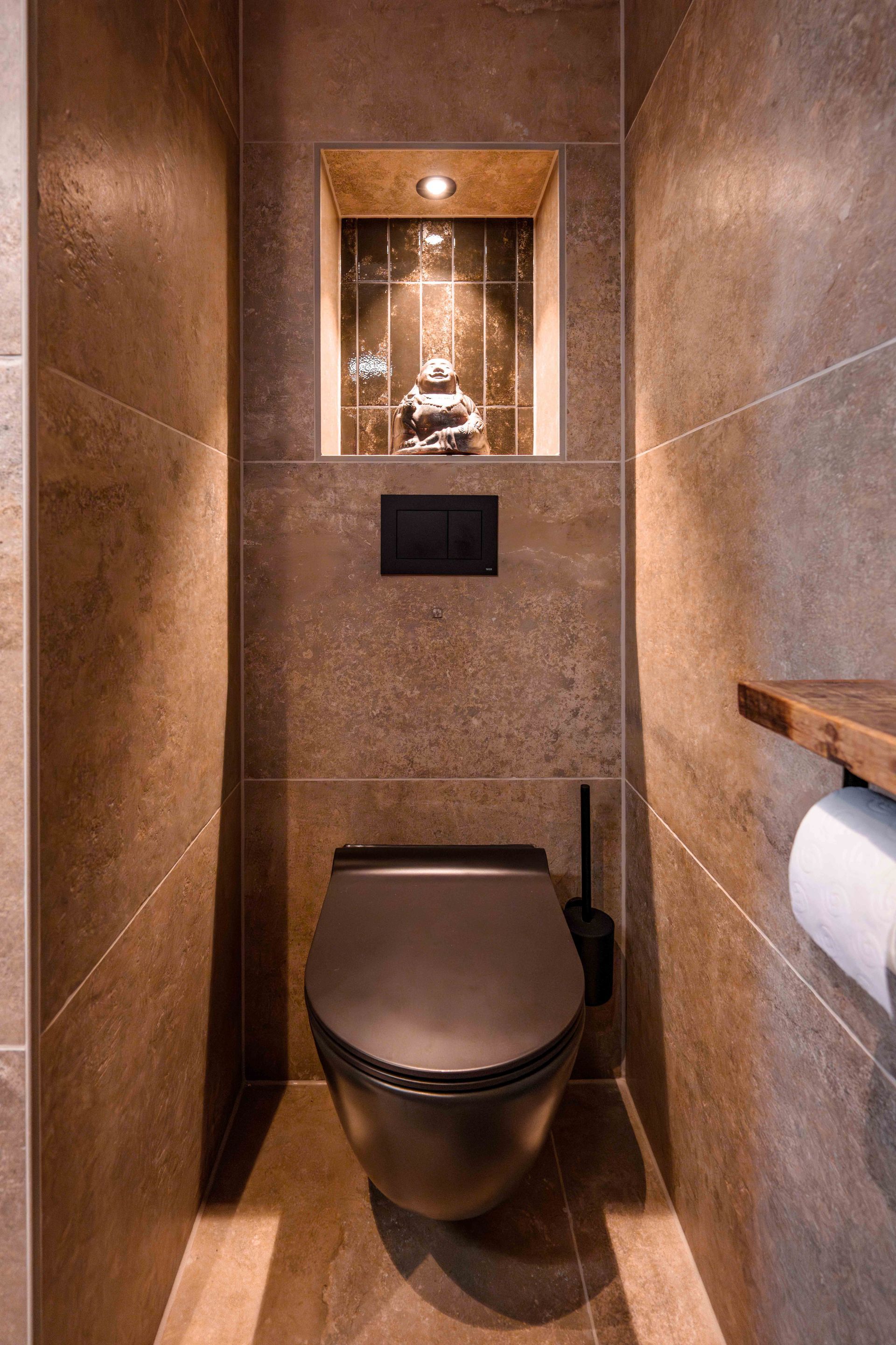 Kleine toiletruimte met bruine tegels, een wandtoilet en een ingebouwde plank erboven.