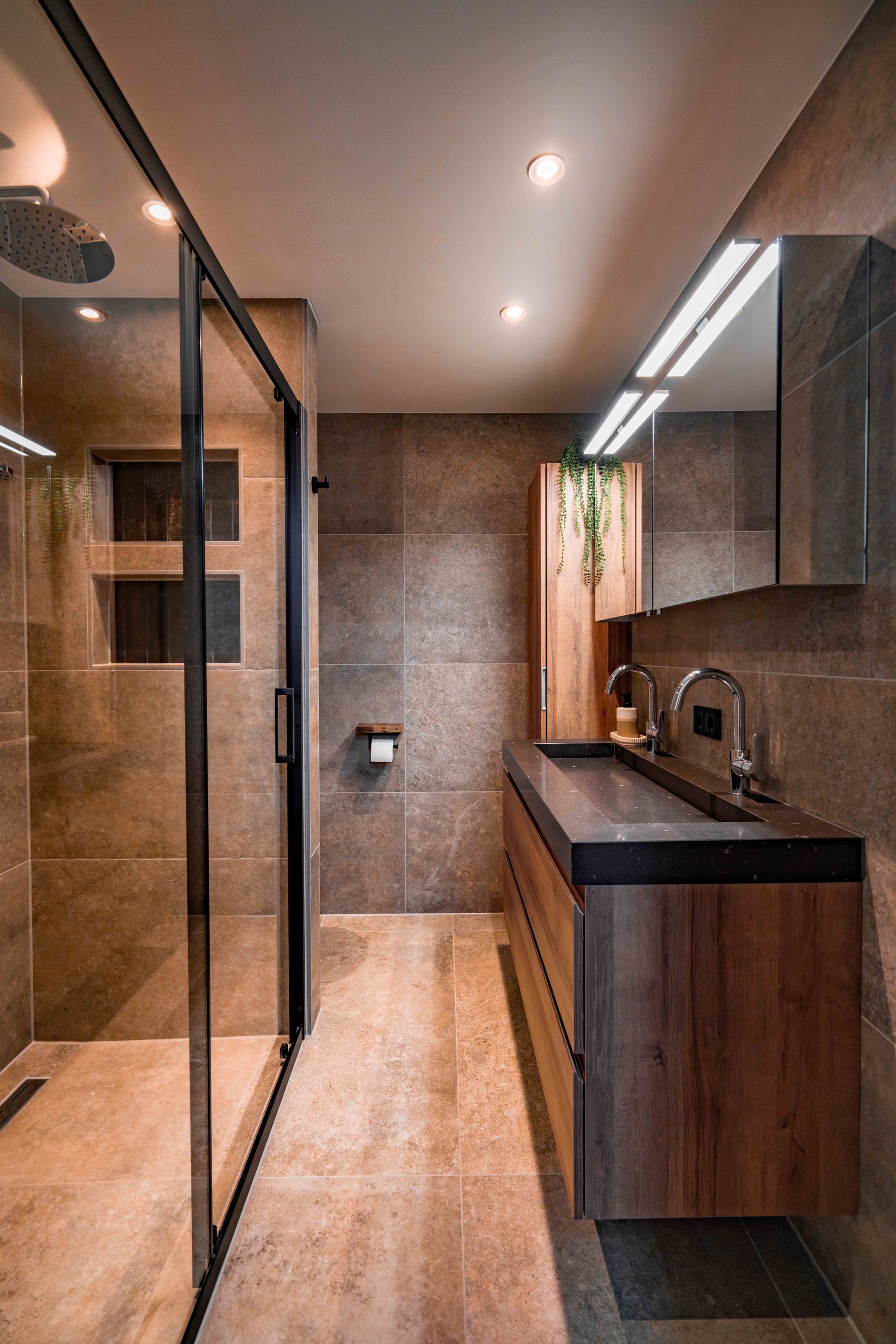 Moderne badkamer met glazen douchecabine, houten wastafelmeubel en sfeervolle inbouwverlichting.