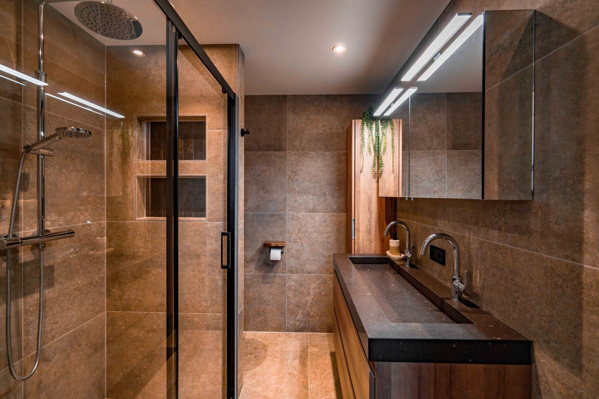 Moderne badkamer met glazen douchecabine, donker badmeubel en bruine tegelwanden.