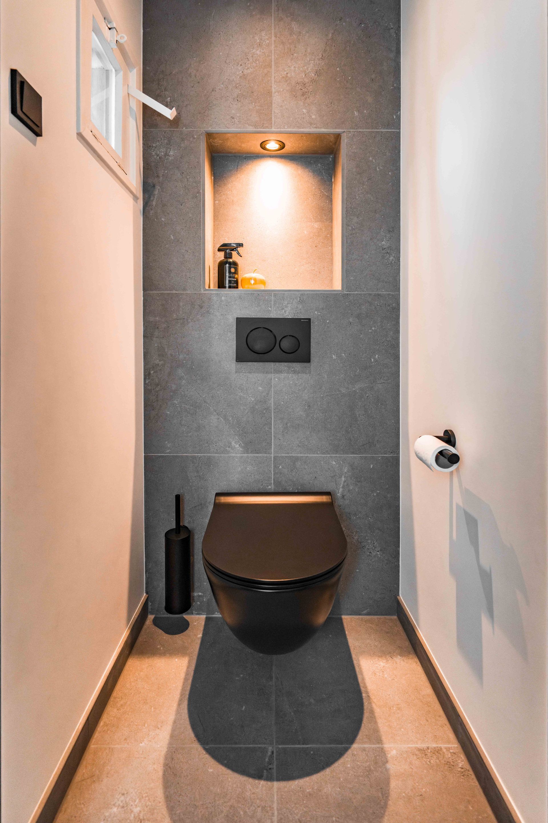 Smalle, moderne badkamer met een wandtoilet, een achterwand bekleed met grijze tegels en een ingebouwde plank met verlichting.