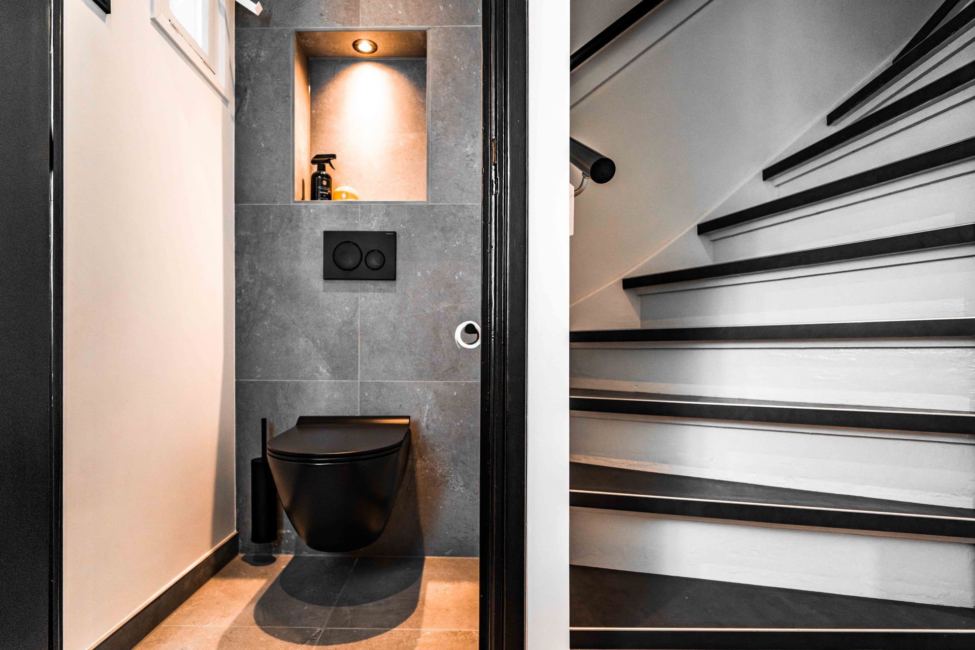 Compacte, moderne badkamer met toilet en wastafel naast een trap met zwarte treden.