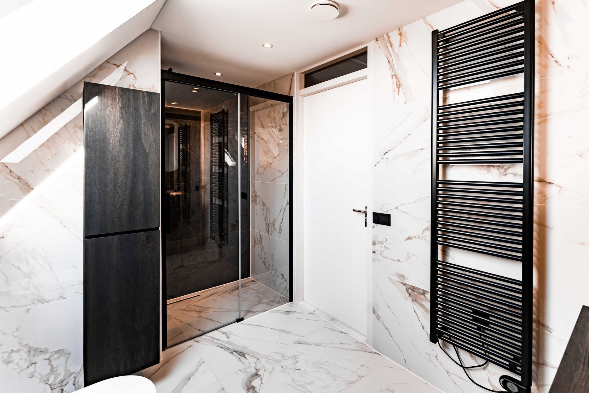 Moderne badkamer met marmeren wanden, glazen douchecabine en een zwarte handdoekradiator aan de rechterkant.