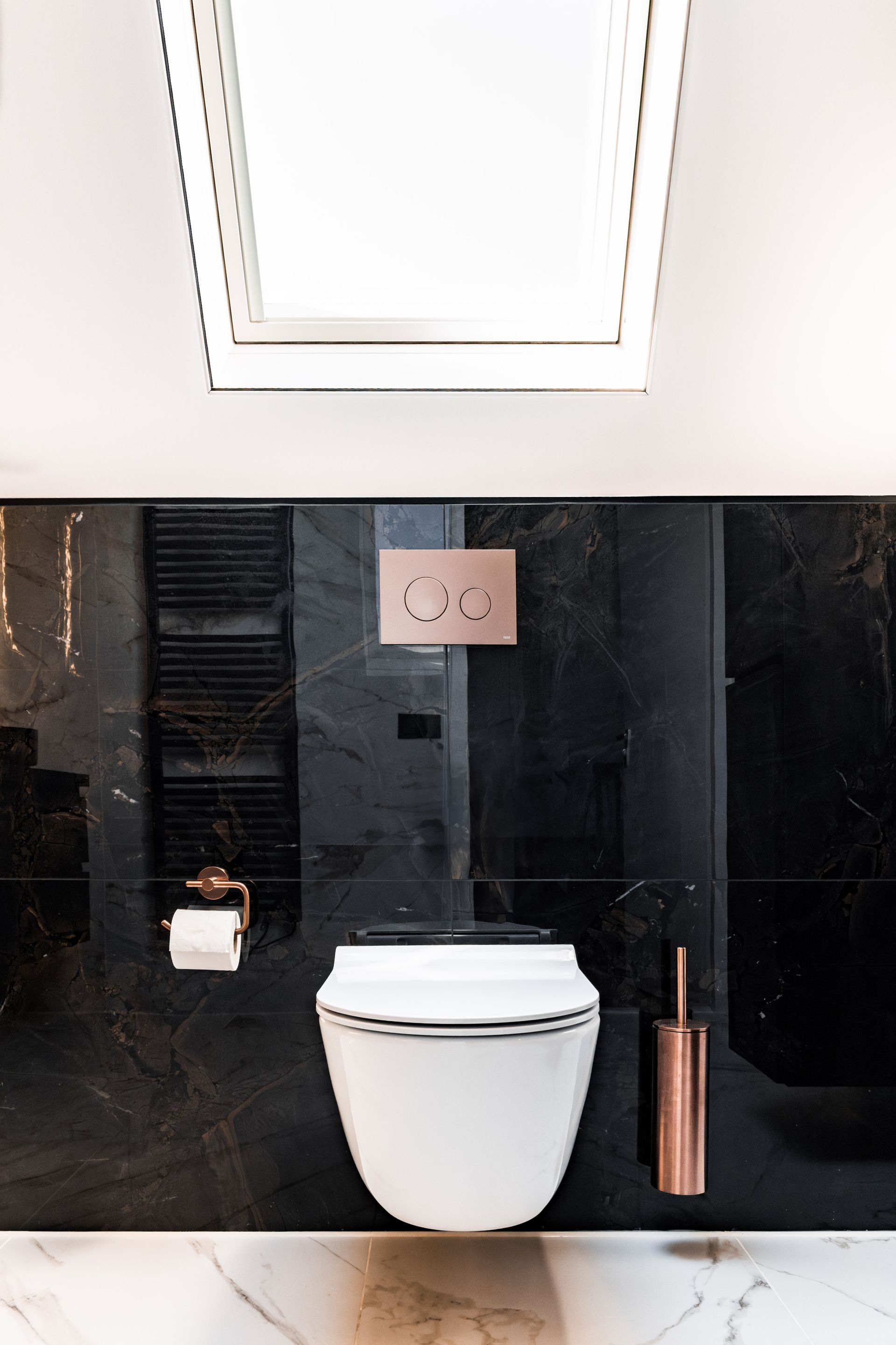 Moderne badkamer met wit toilet, zwarte tegelwand en ingebouwde plank met toiletborstel en ontstopper.