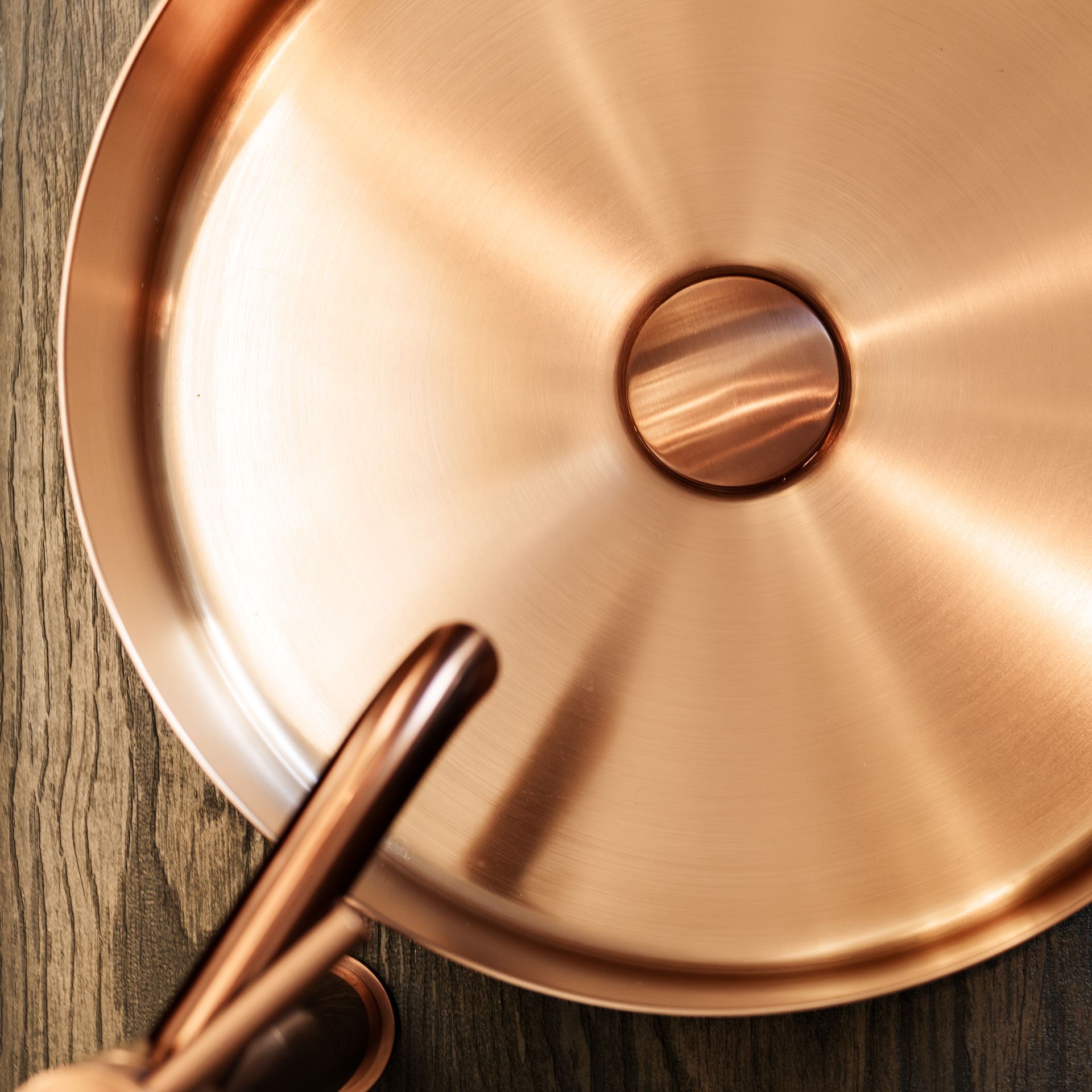 Koperen deksel voor een steelpan met een houten handvat op een rustieke houten ondergrond.