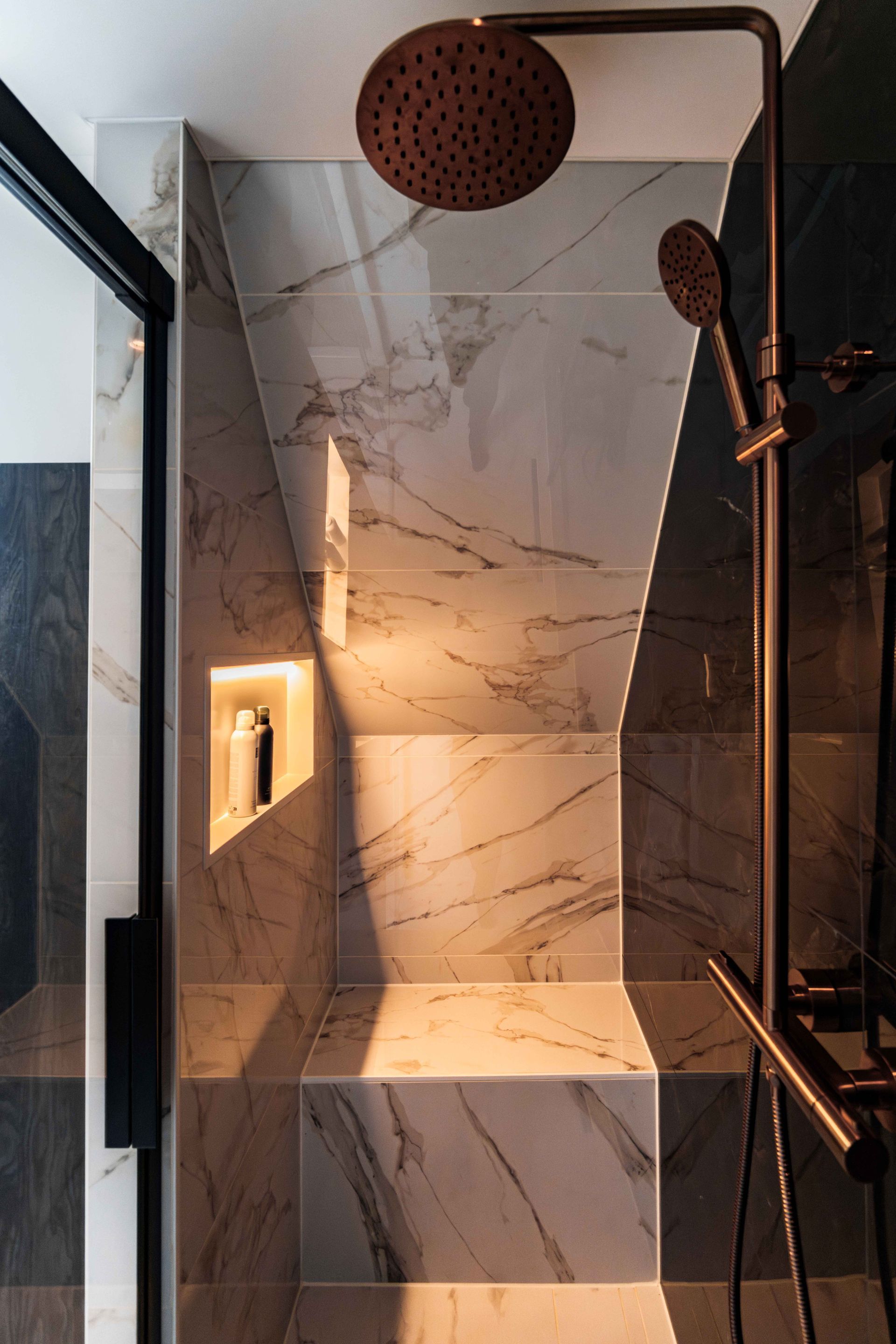 Moderne douche met marmerlook tegels, donkere kranen en ingebouwde plankverlichting.