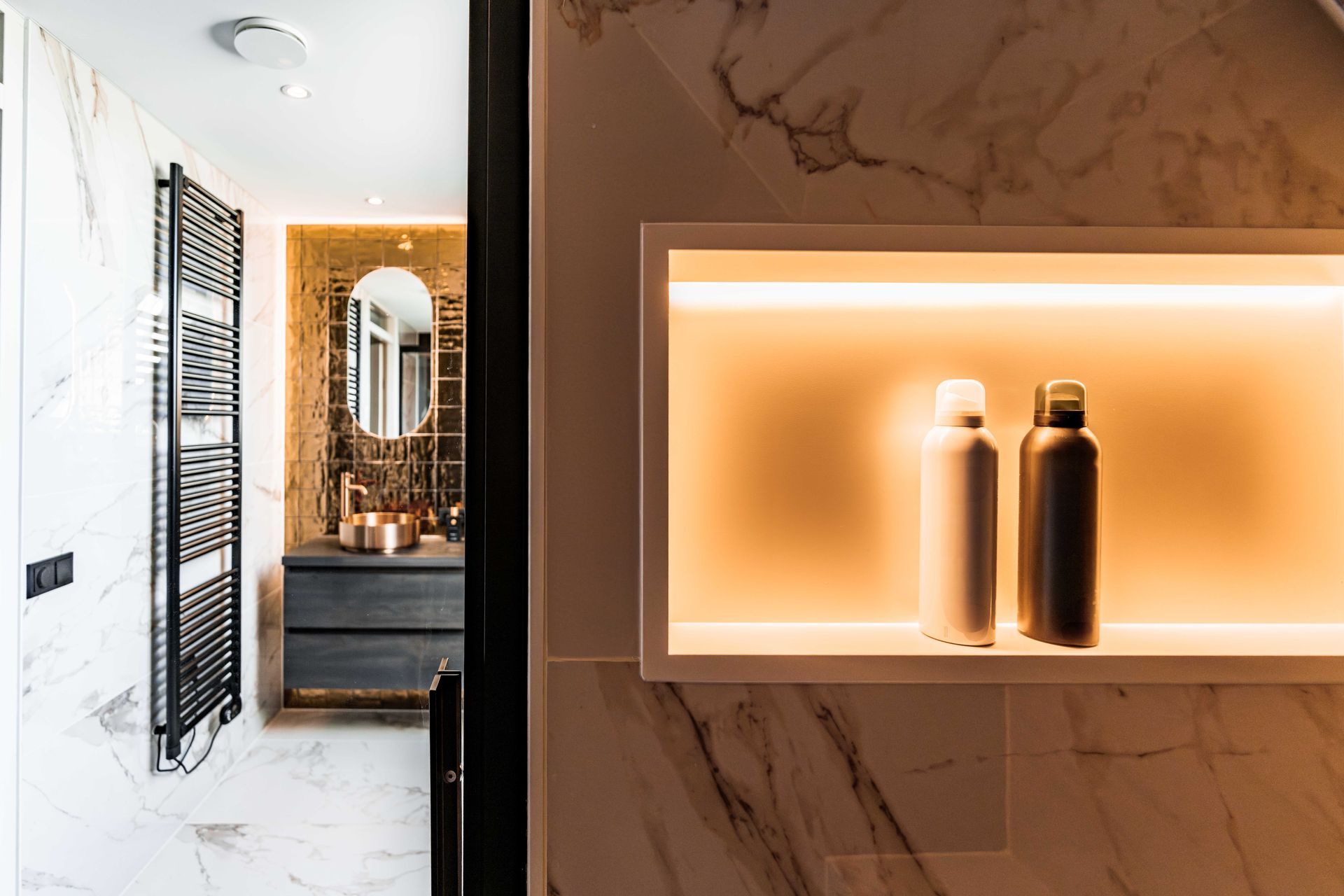 Luxe badkamer met marmeren muren, een verlichte plank en twee flessen naast een make-upspiegel.