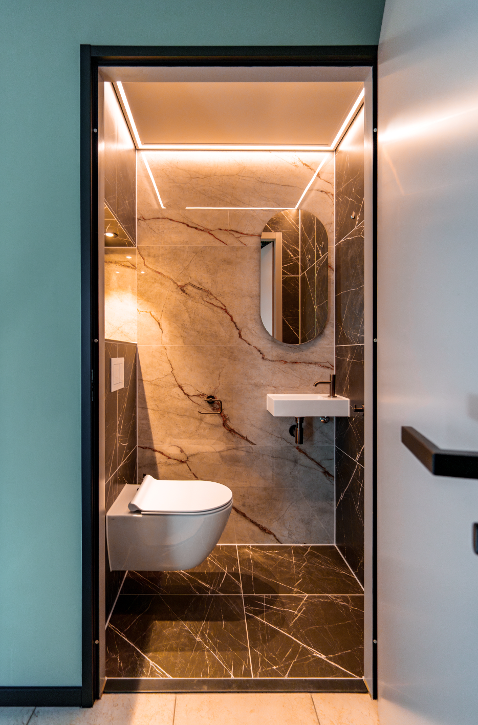 Moderne badkamer met marmeren wanden, wandtoilet, wastafel en sfeervolle led-plafondverlichting.