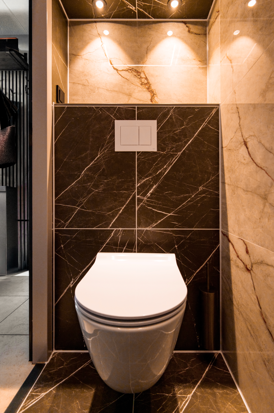Moderne badkamer met een wandtoilet, donkere marmeren tegels en warme verlichting.