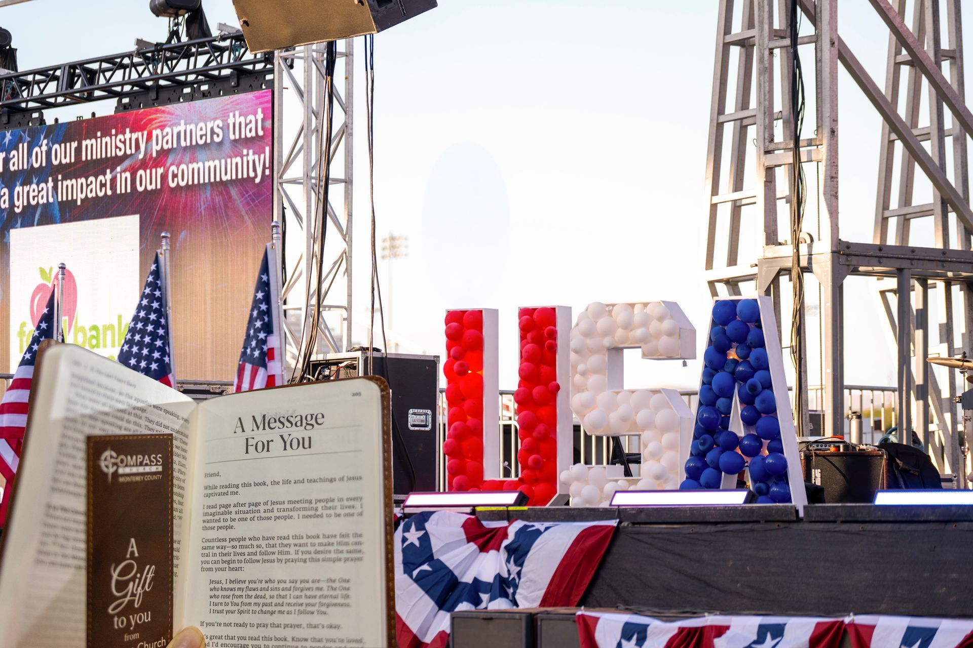 Memorial stage with red, white, and blue decorations and large block letters, with an open book display in front