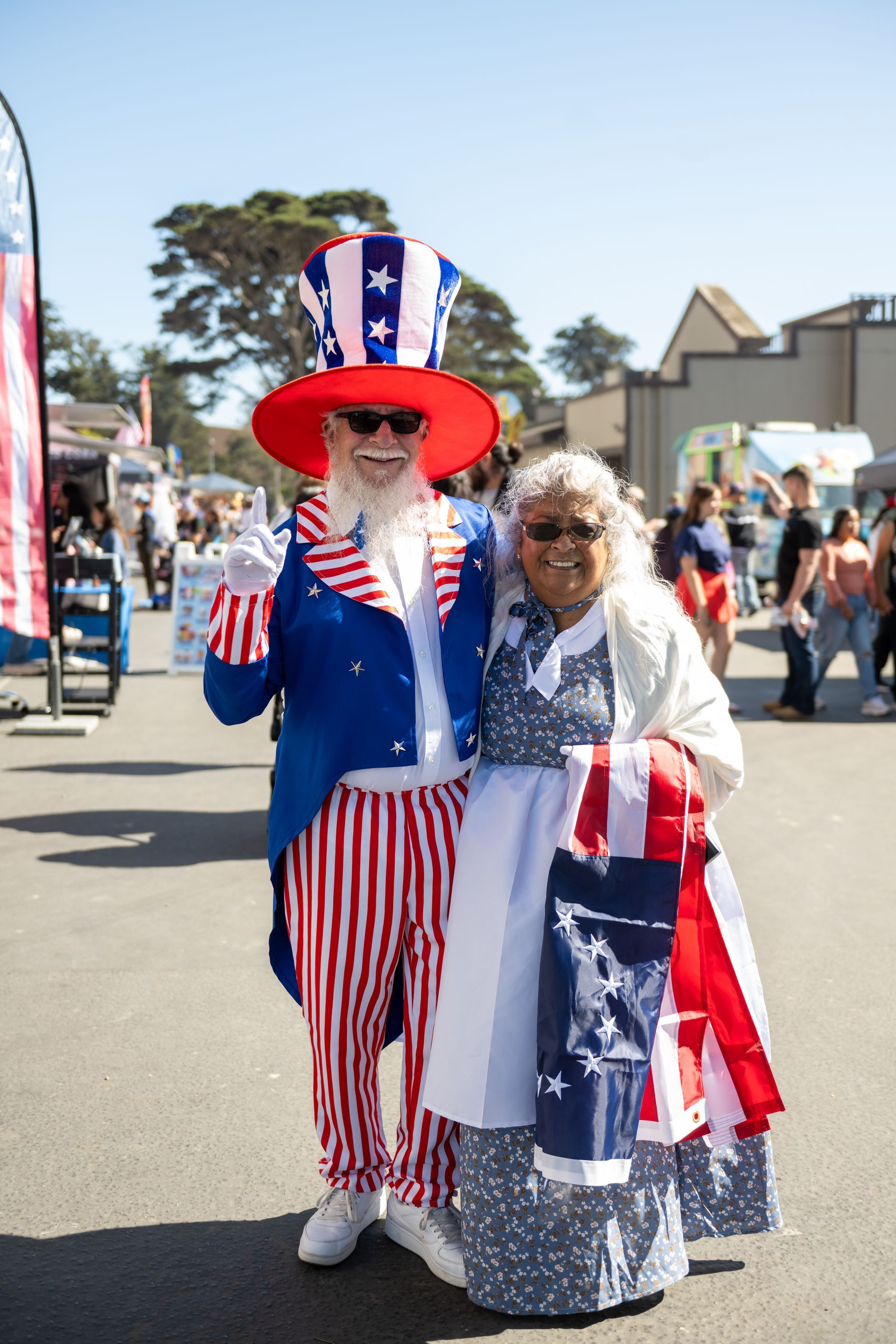 Person dressed as Uncle Sam poses with another in a patriotic costume at an outdoor event.