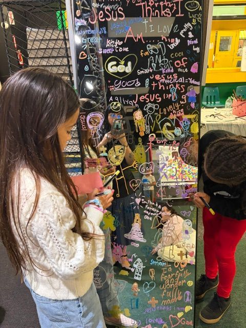 Two children placing notes on a colorful graffiti-covered wall in an outdoor street art area