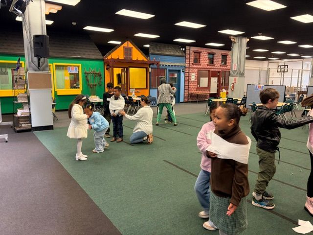 Children playing in an indoor play area with colorful house facades and a green carpeted floor