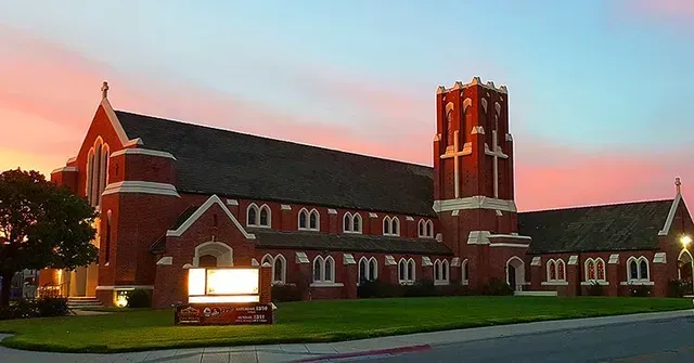 Padre Brick church building with a tower against a sunset sky.