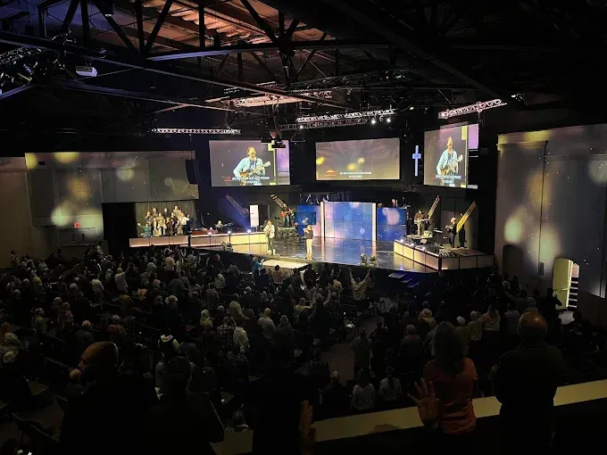 Audience watching a church service with a band on stage. People are raising their hands.