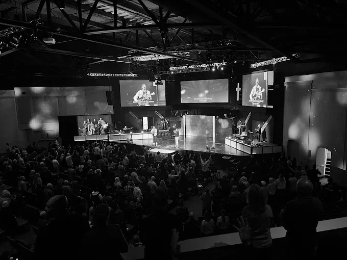 Black and white photo of a large church service. Stage with band, screens, and a crowd of people at Compass Church, Salinas]