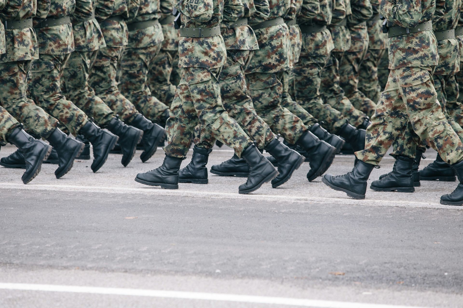 Soldiers in camouflage uniforms marching in unison on a gray road.