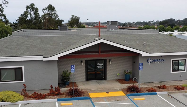 Gray building with a dark brown entryway, a sign that reads COMPASS, and a handicapped parking spot.