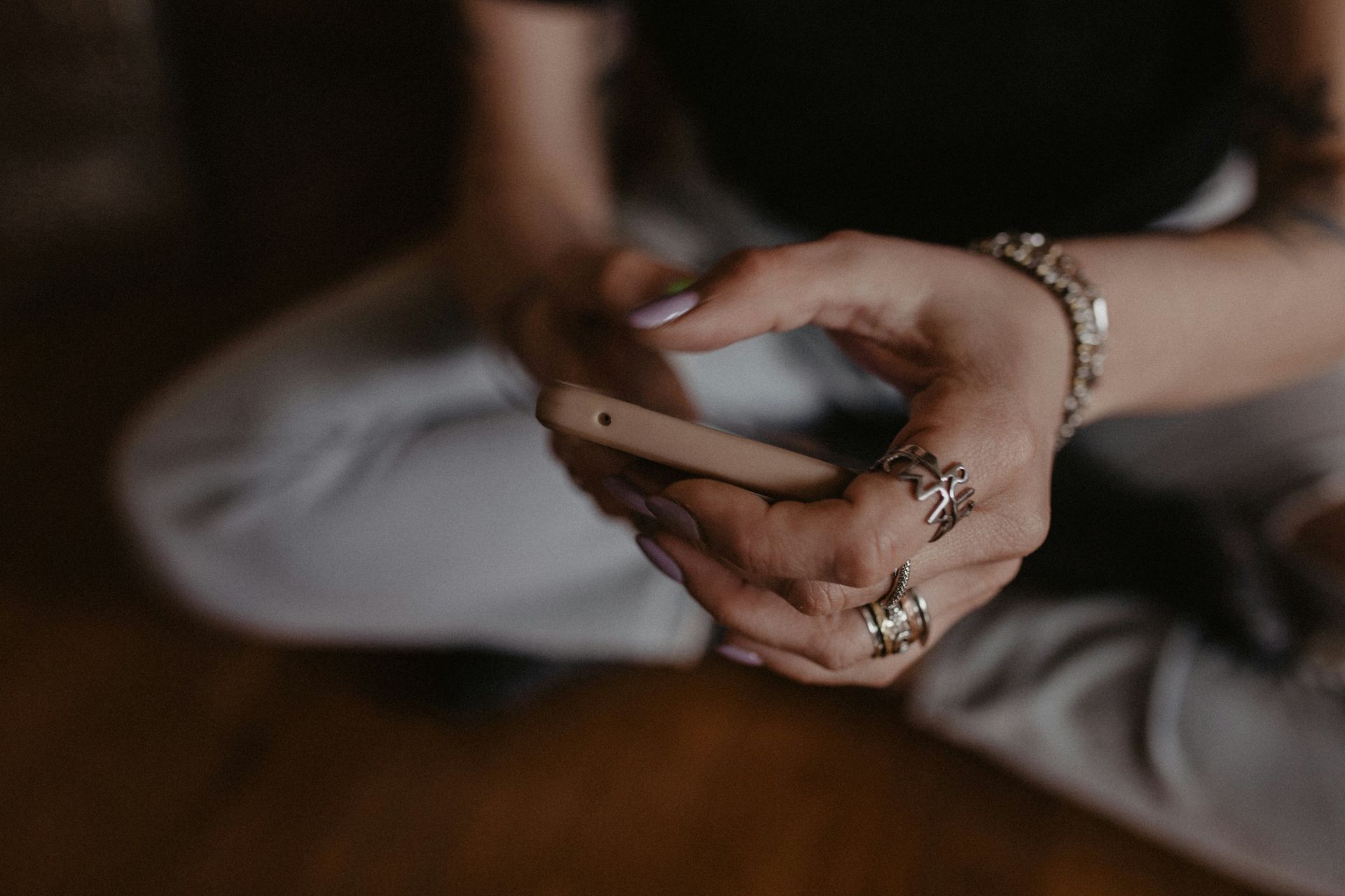 A person's hands holding a phone, wearing rings and bracelets. They are sitting down.