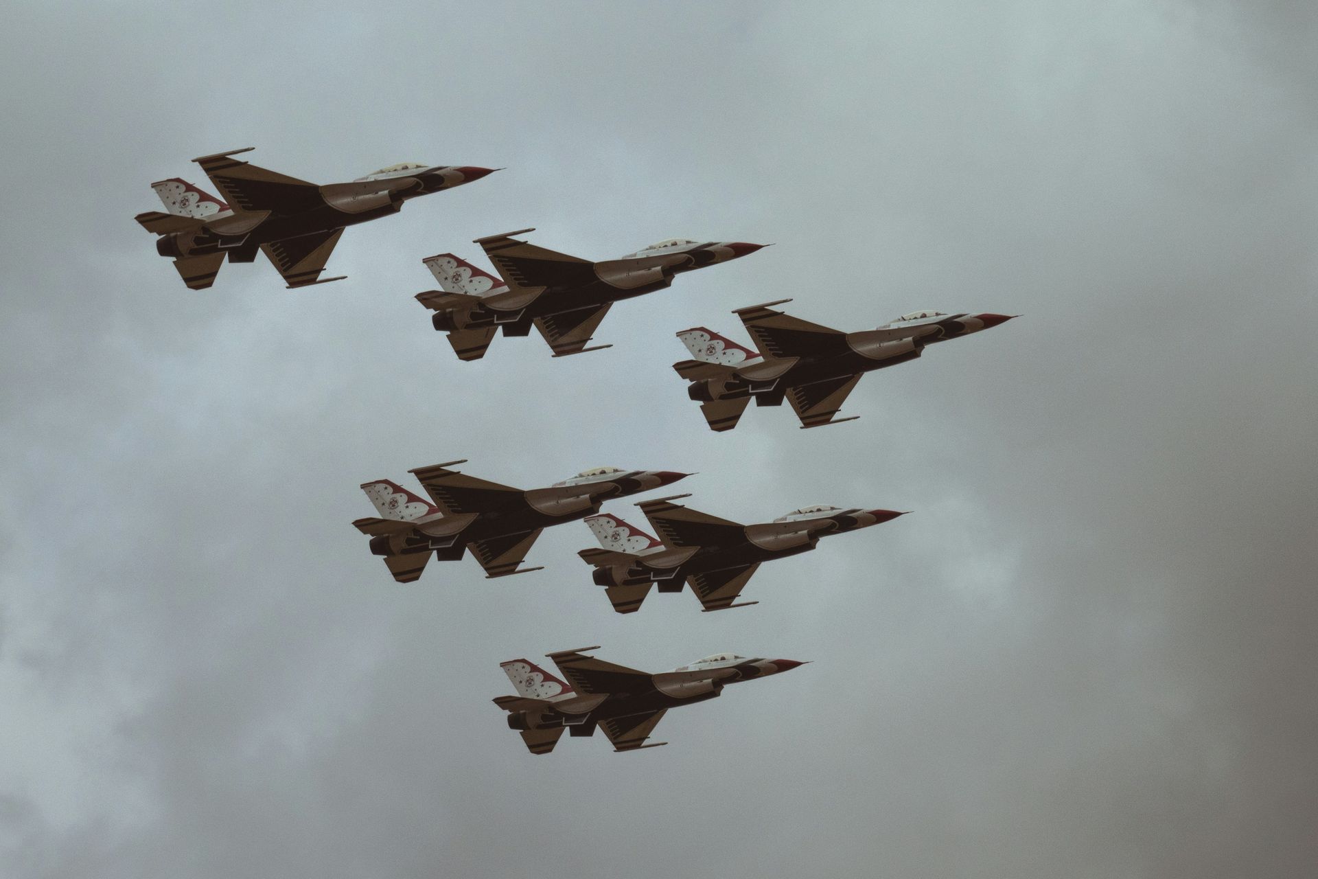 Seven fighter jets flying in formation against a cloudy sky.