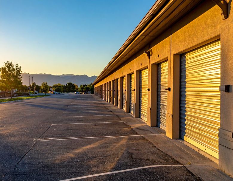 Sunlit row of closed storage unit garage doors beside an empty parking lot at sunset