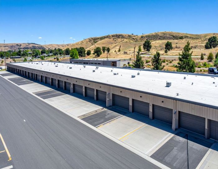 Long industrial warehouse with white roof and loading docks beside an empty paved lot