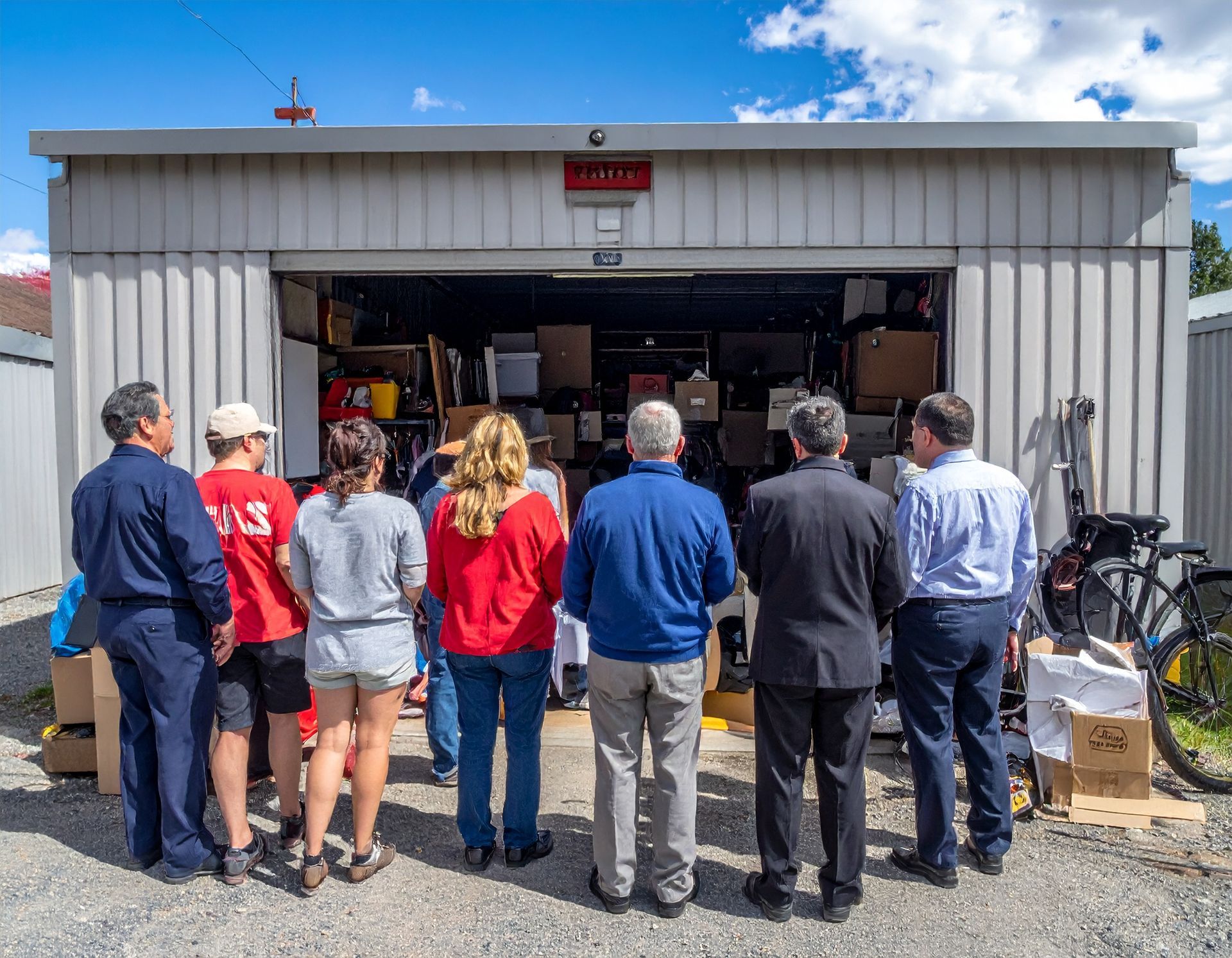 People gathered outside a garage looking into shelves and equipment inside.